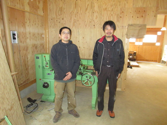 丸嘉小坂漆器店の小坂玲央さん（左）と納品させて頂いた北産の倣い旋盤の前で